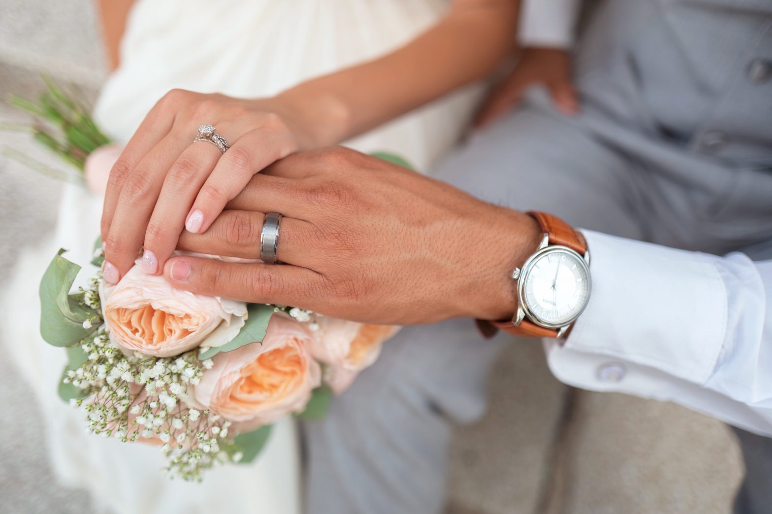 Hands of a man and a woman wearing wedding rings resting on a bouquet
