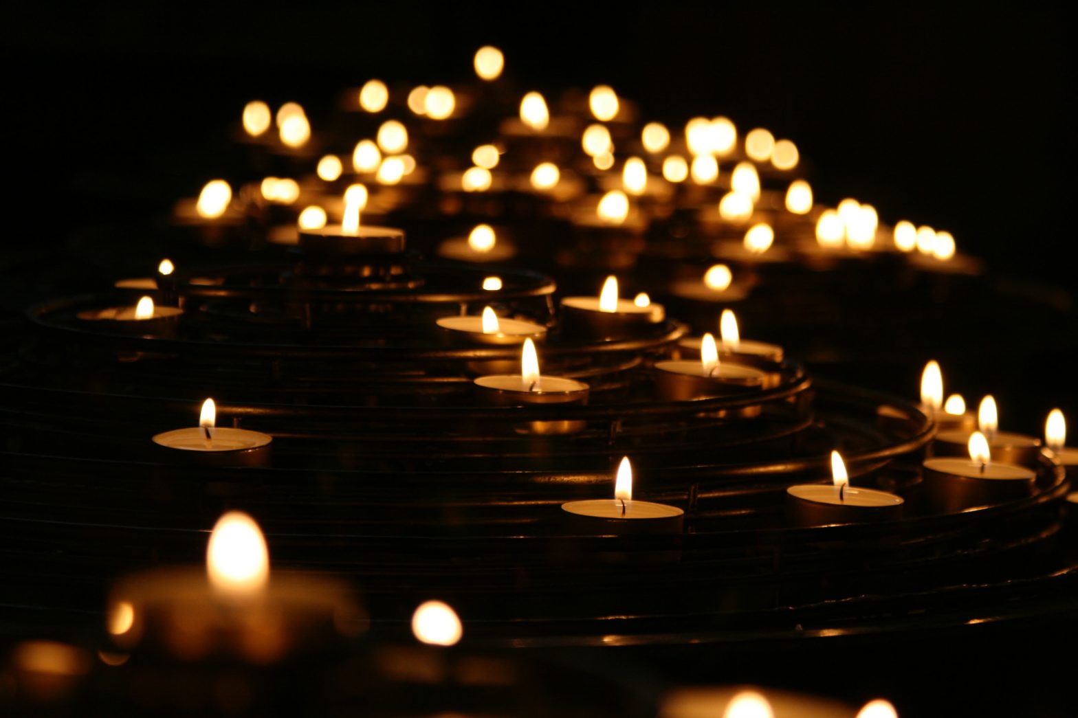 Many lit tea light candles in a dark room