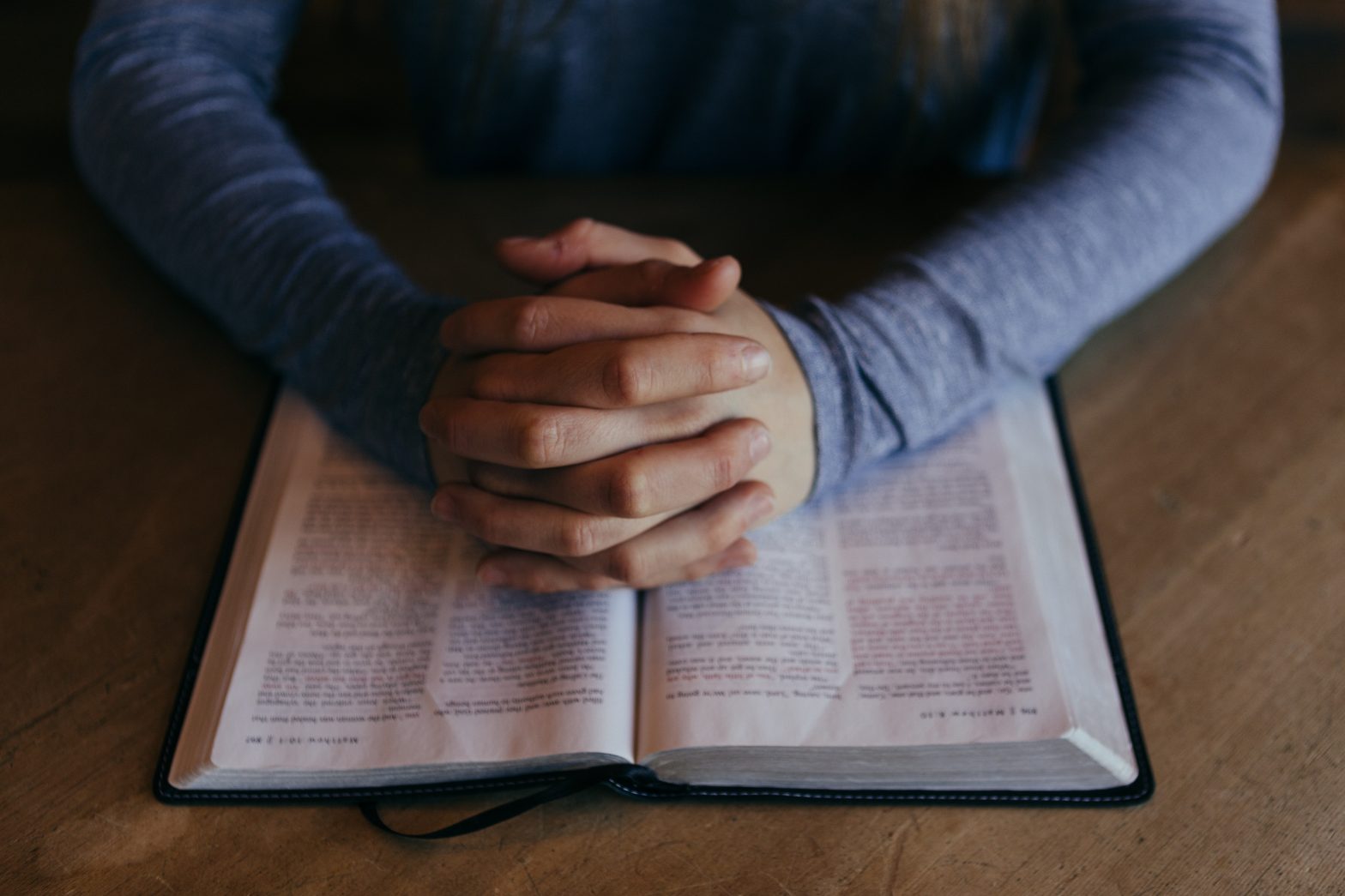 Hands with enclosed fingers rest on an open Bible.