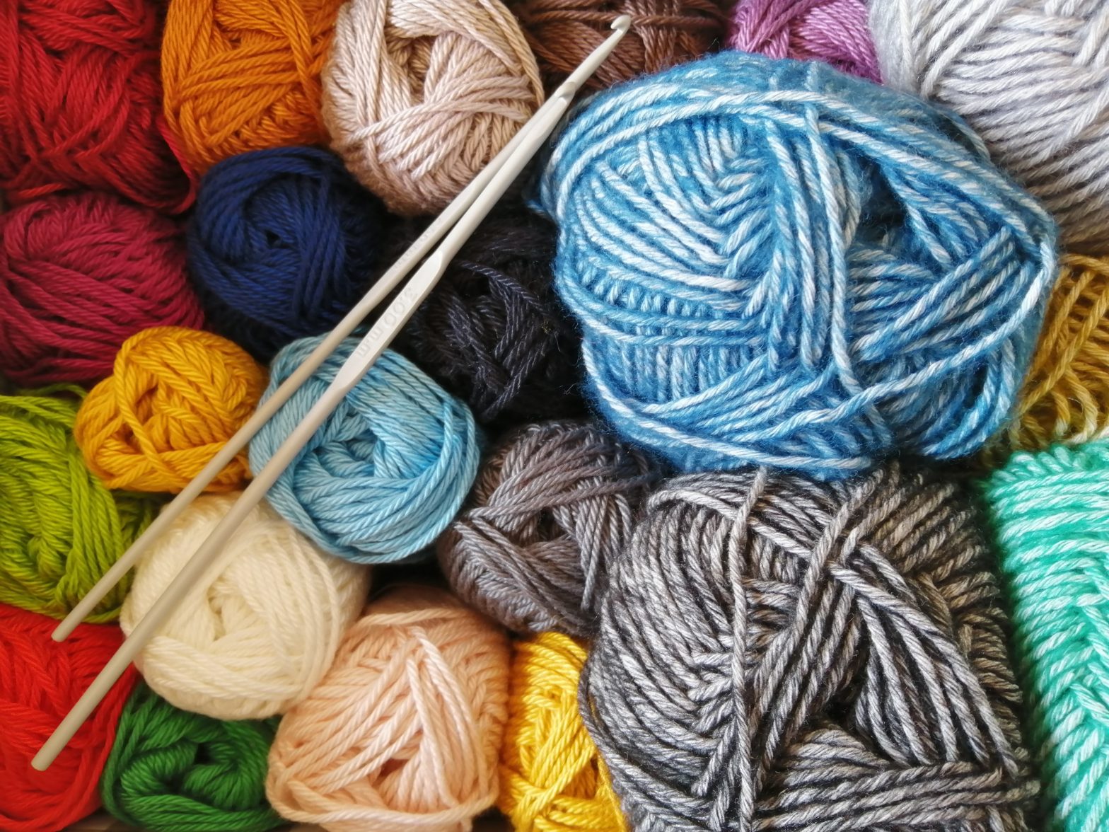 Various different coloured balls of wool with two knitting needles resting on top.